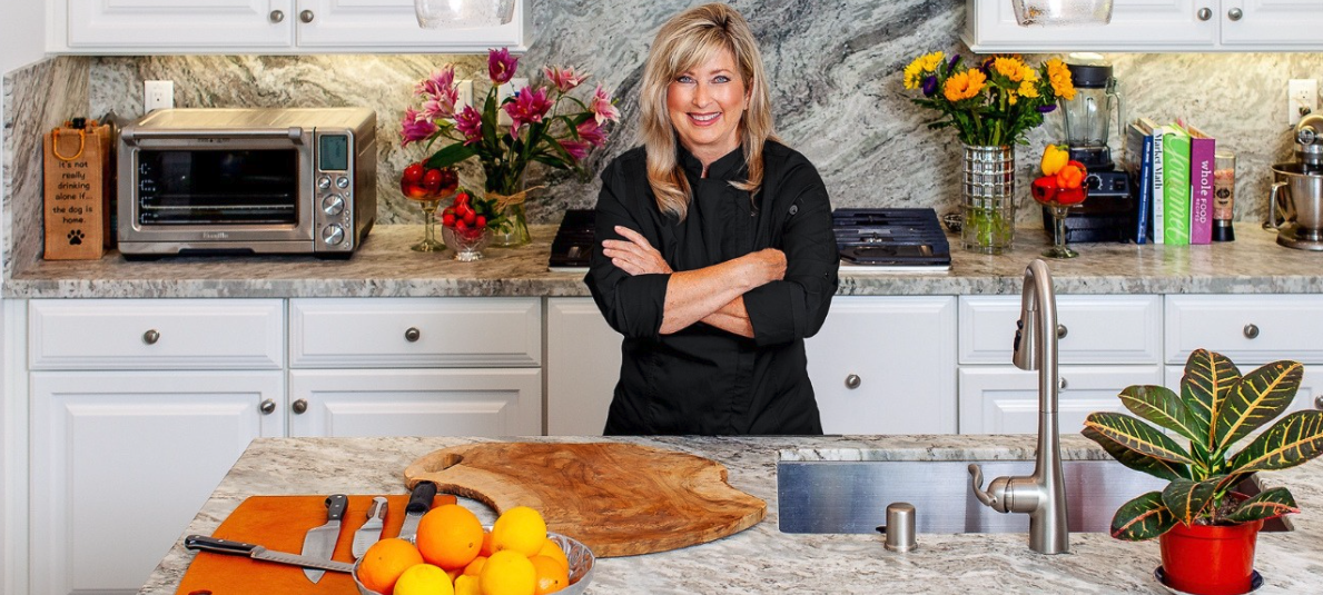 Lisa Redman in her kitchen wearing a chef's coat, surrounded by fresh flowers and produce