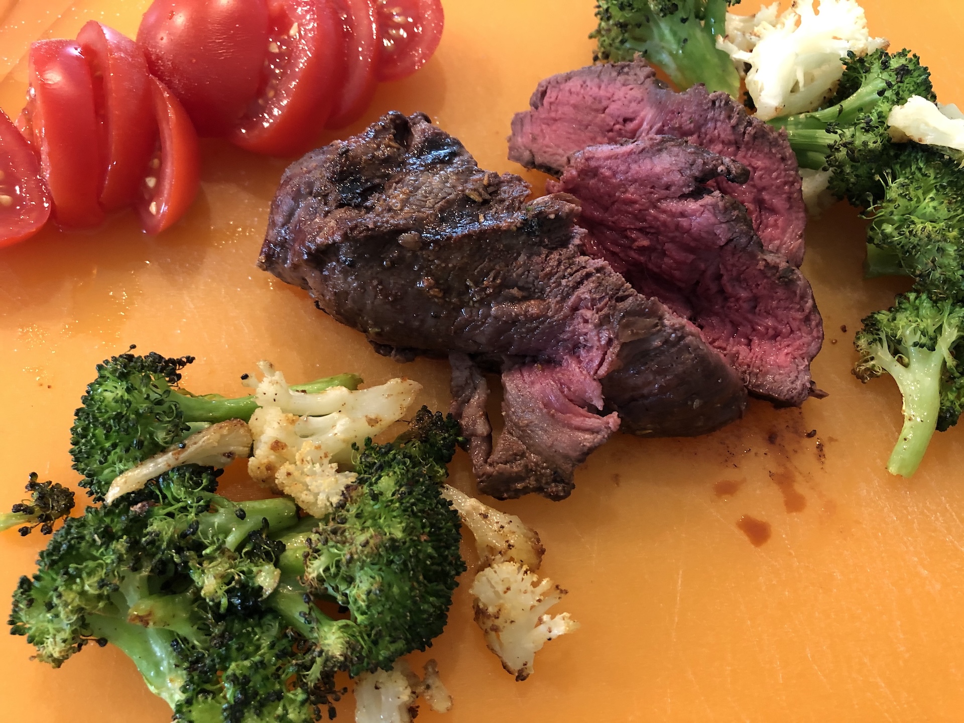 Sliced steak with roasted broccoli and tomato on a cutting board